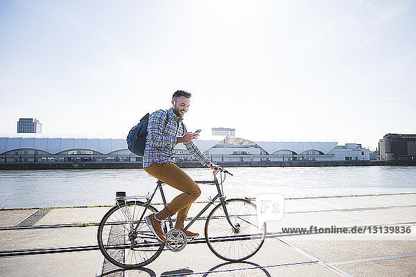 Happy man using phone while cycling by canal against clear sky