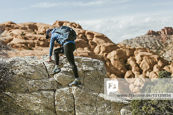 Wanderin mit Rucksack klettert bei Sonnenschein an Felsen