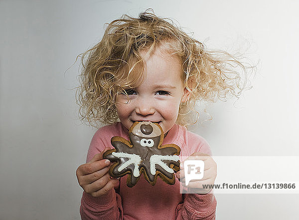 Portrait of girl holding cookie while standing against white wall at home