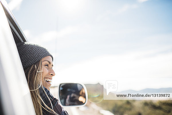 Lächelnde junge Frau fährt im Auto gegen den Himmel