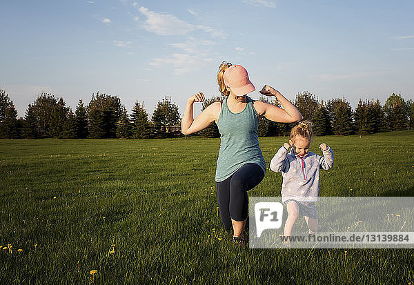 Mutter mit Tochter trainiert auf Grasfeld im Park gegen den Himmel bei Sonnenuntergang