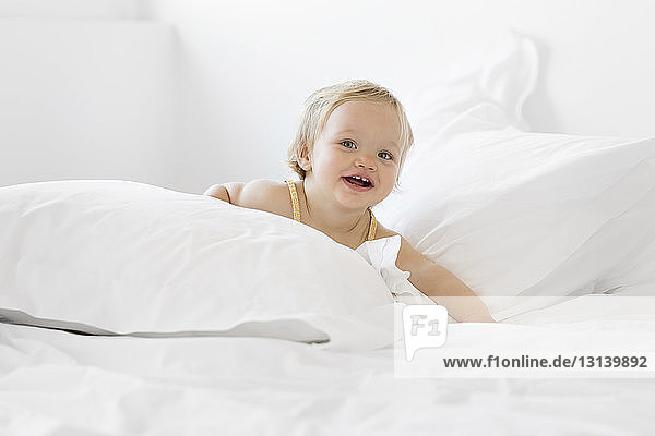 Porträt eines glücklichen kleinen Mädchens  das zu Hause auf dem Bett liegt