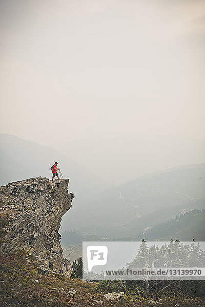 Mitteldistanzansicht eines Wanderers  der bei nebligem Wetter auf einer Klippe gegen Berge und Himmel steht