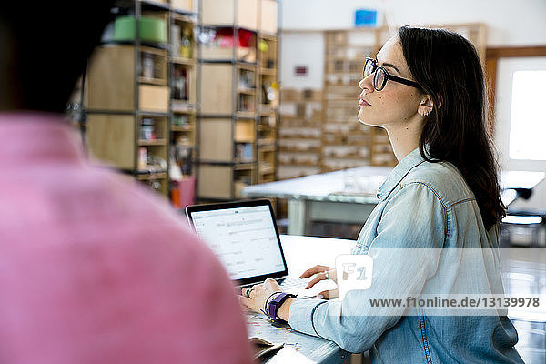 Geschäftsfrau schaut weg  während ein männlicher Kollege einen Laptop benutzt