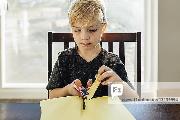 Junge schneidet zu Hause Papier mit einer Sicherheitsschere