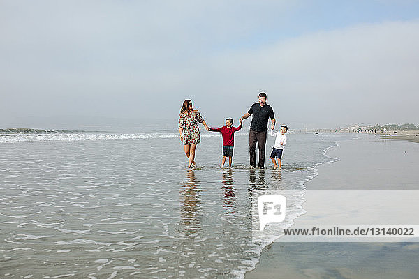 Family holding hands while walking on shore at beach against sky