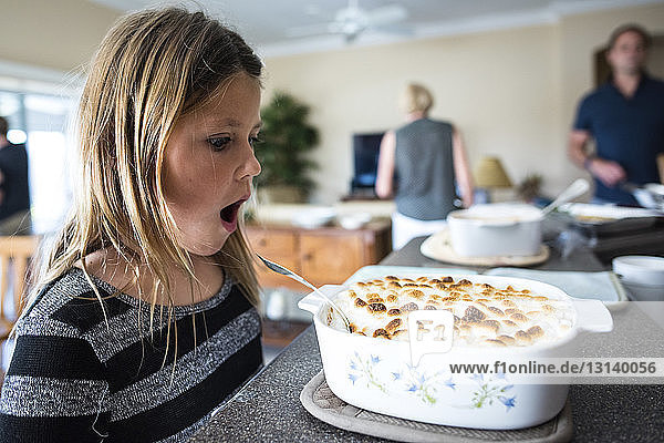 SurPRised girl looking at desert in container with parents in background at home
