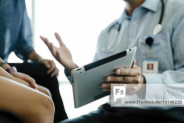 Abgetrennte Hand eines Kinderarztes  der Mutter und Tochter im Untersuchungsraum einen Tablet-Computer zeigt