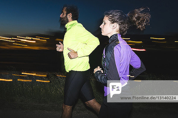 Seitenansicht eines jungen Paares  das in der Nacht auf einem Fußweg joggt