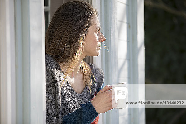 Thoughtful woman holding mug while standing at window