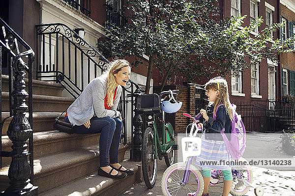 Cheerful mother and daughter with bicycles talking on steps