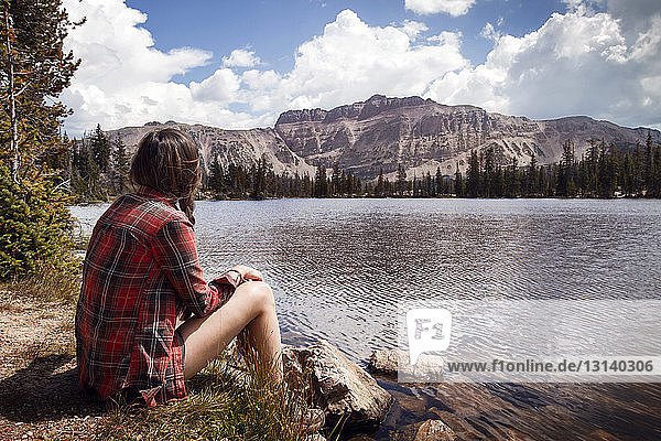 Nachdenkliche Frau sitzt am Seeufer im Wald