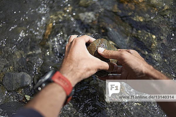Abgehackte Hände eines Wanderers beim Pflücken von Steinen aus fließendem Fluss