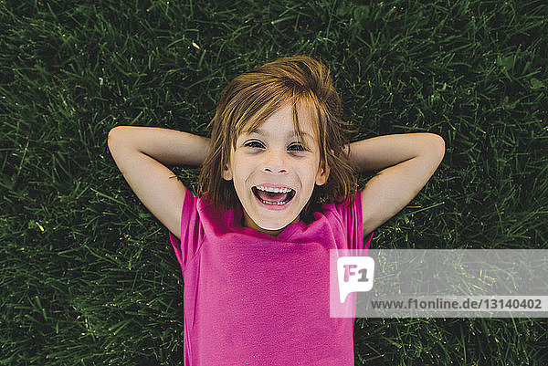 Overhead portrait of cheerful girl with hands behind head while lying on grassy field
