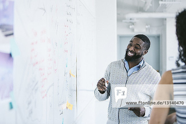 Lächelnder Geschäftsmann betrachtet Whiteboard  während er einen Tablet-Computer im Büro hält