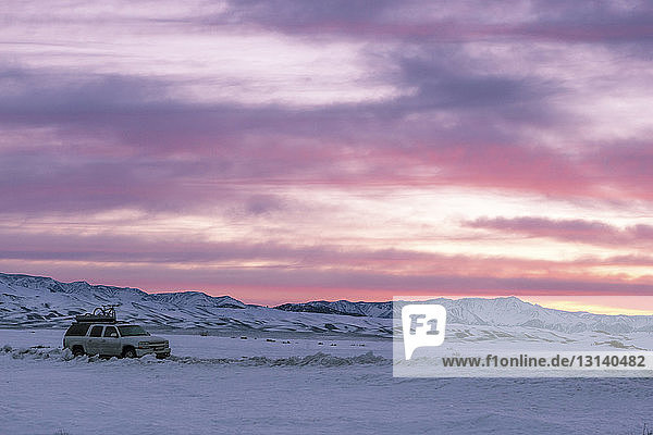Hochwinkelansicht eines Geländewagens auf verschneitem Feld vor dramatischem Himmel
