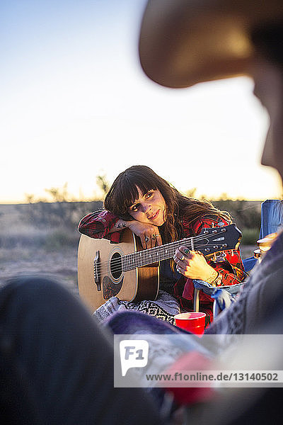 Frau lehnt auf Gitarre  während sie auf Feld gegen Himmel sitzt