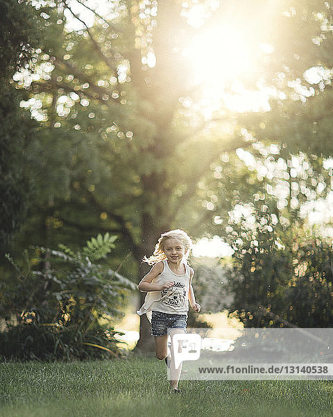 Happy girl running on grassy field against trees during sunny day