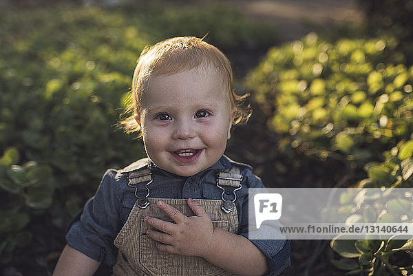 Porträt eines glücklichen kleinen Jungen  der bei Sonnenuntergang im Park vor Pflanzen steht