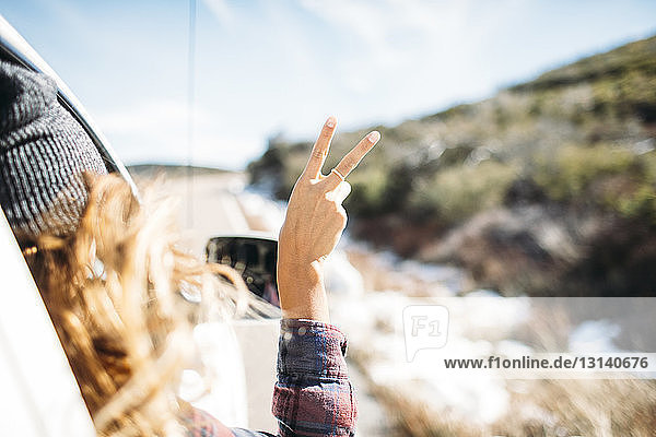 Rückansicht einer Frau  die im Auto sitzend ein Friedenszeichen gestikuliert