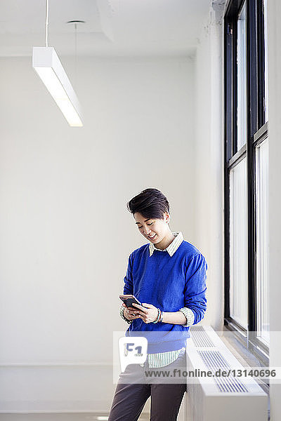 Businesswoman using mobile phone while standing by window in new office