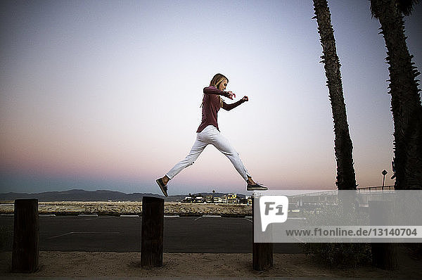 Side view of woman jumping on wooden posts in city