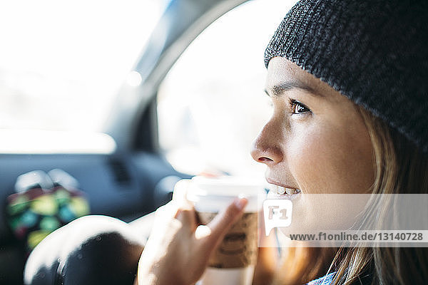 Nahaufnahme einer jungen Frau  die im Auto sitzend eine Kaffeetasse hält