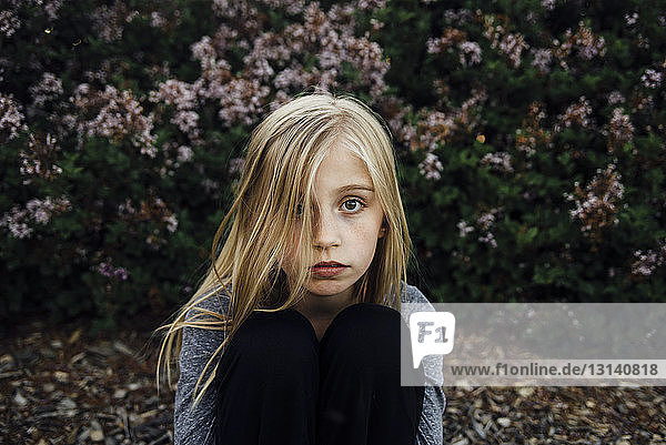 Porträt eines Mädchens  das im Park vor Pflanzen sitzt