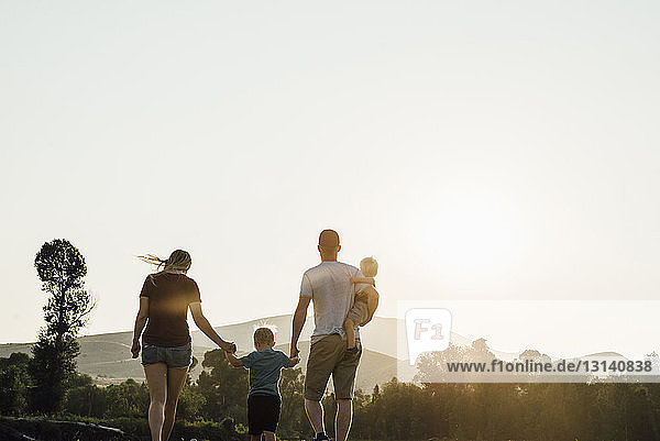 Familie geht bei Sonnenuntergang gegen klaren Himmel auf dem Feld