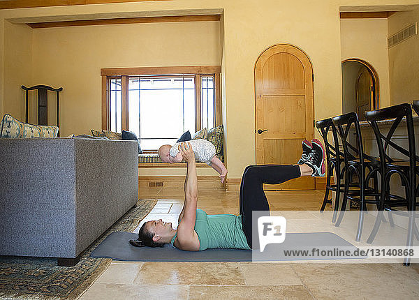 Side view of happy mother exercising with daughter on exercise mat at home