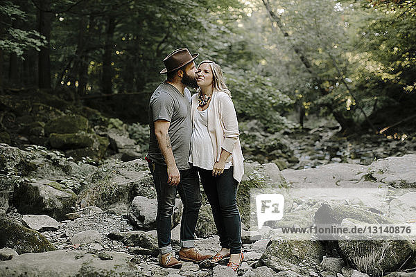 Seitenansicht eines Mannes  der seine Frau küsst  während er auf Felsen im Wald steht