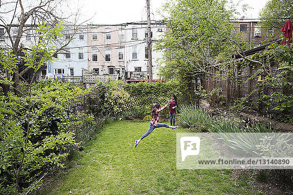 Girl photographing sister in mid-air over grass in yard