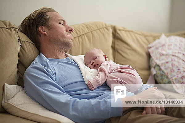 Father with baby girl sleeping on sofa at home