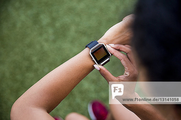 Hochwinkelaufnahme einer Sportlerin mit einer intelligenten Uhr  die auf einem Rasenfeld steht