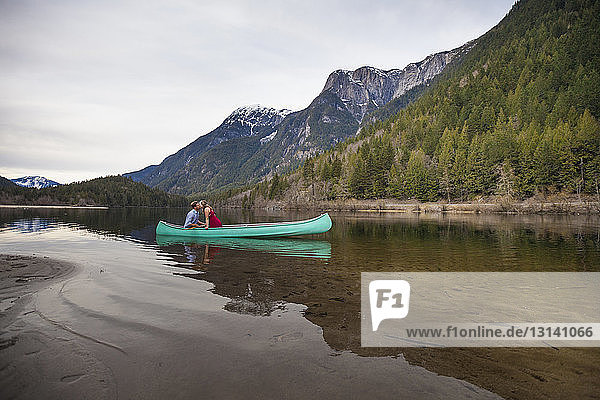 Young couple sitting in canoe on lake against mountains
