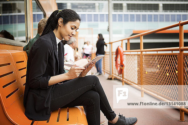 Smiling woman using digital tablet while sitting on bench in city