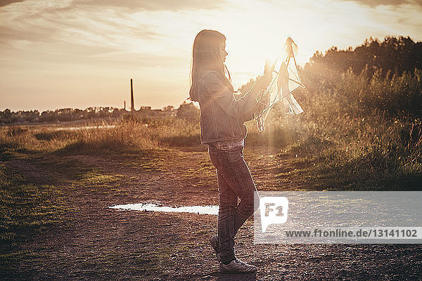 Girl holding kite and standing on field against sky on sunny day