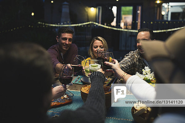 Friends toasting wineglasses while sitting at table during dinner party