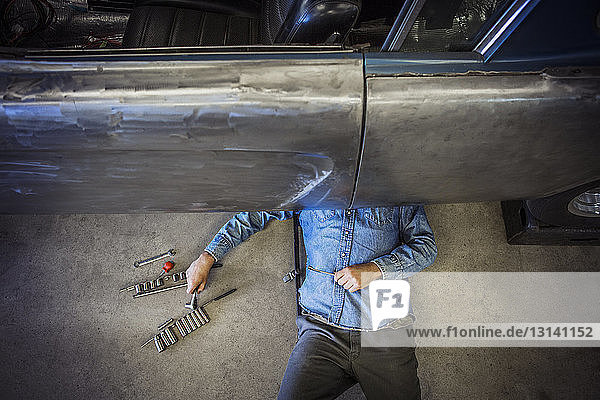 Draufsicht eines Mechanikers  der in einer Autowerkstatt unter dem Auto arbeitet
