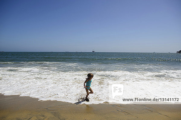 Verspieltes Mädchen rennt am Strand von Seal Beach gegen den klaren Himmel auf Surfbrettern