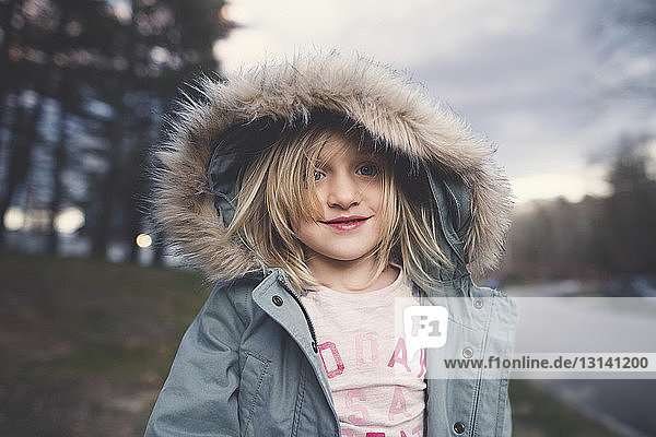 Cute smiling girl wearing fur hood standing on field