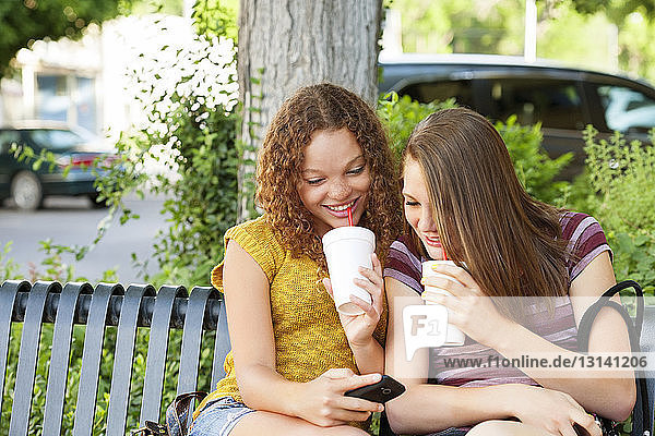 Teenager-Mädchen zeigt Mobiltelefon einer Freundin im Park