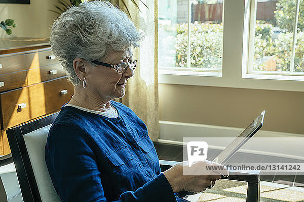 Ältere Frau benutzt Tablet-Computer  während sie sich zu Hause auf einem Stuhl entspannt
