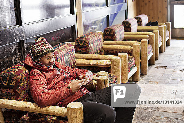 Man using mobile phone while relaxing on armchair at ski resort