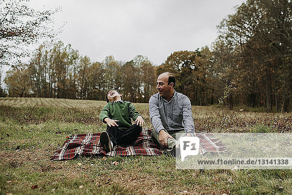 Glücklicher Vater mit Sohn sitzt im Park auf einer Decke gegen den Himmel
