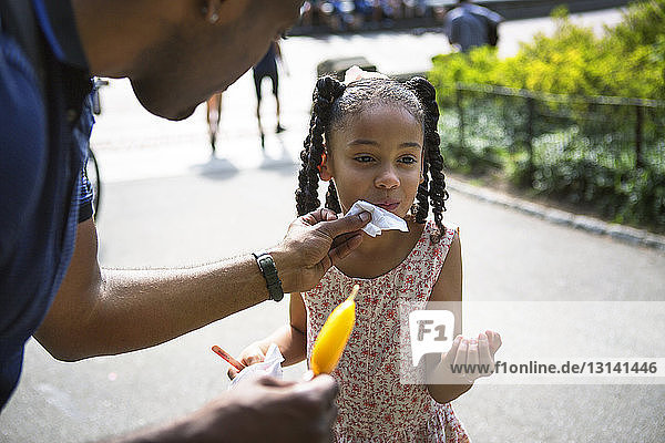 Father cleaning face of daughter with tissue at park