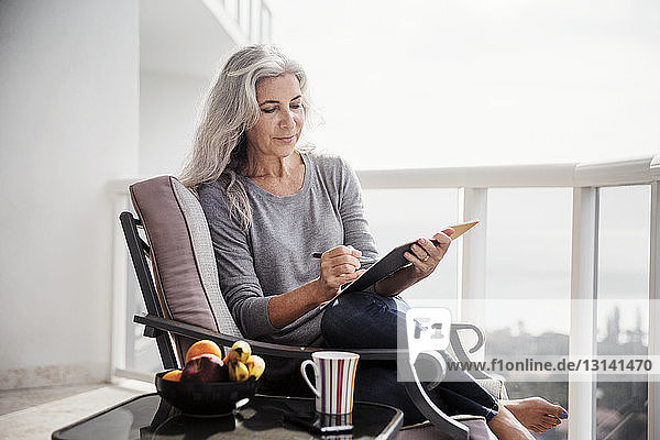 Mature woman writing in book while sitting on chair on balcony