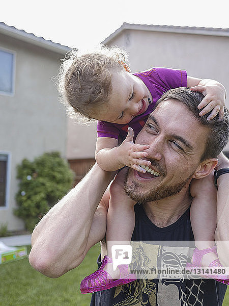 Nahaufnahme eines glücklichen Vaters  der seine Tochter auf den Schultern trägt  während er im Hof steht