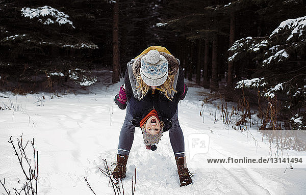 Happy mother playing with daughter while standing in forest during winter
