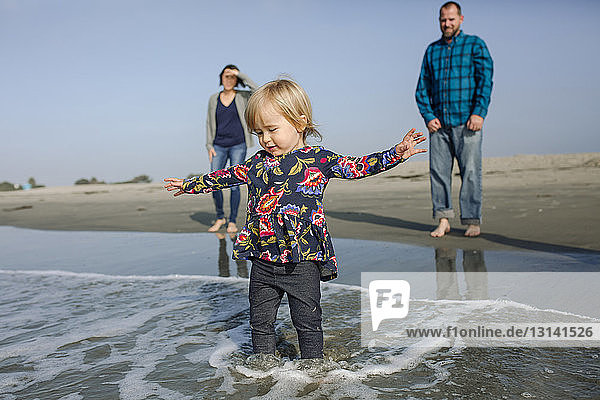 Eltern betrachten Tochter beim Spielen in Wellen am Strand am Ufer